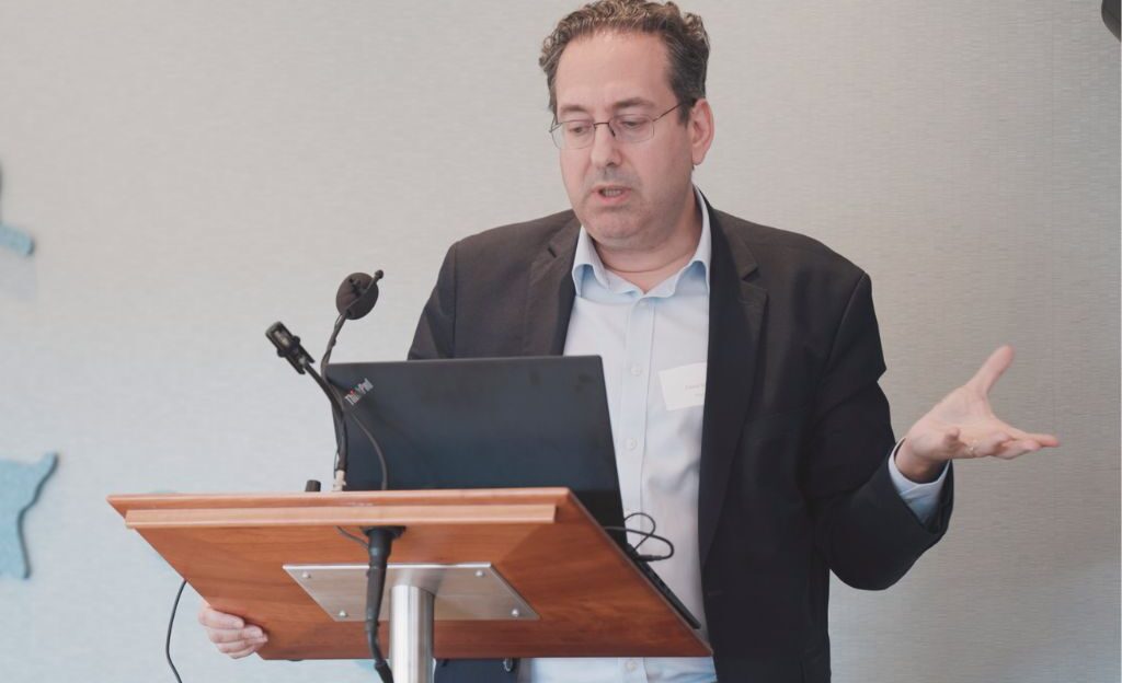 David Silagy stands at lectern with laptop, gesticulating animatedly