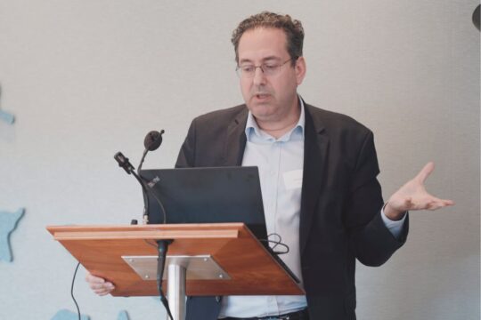 David Silagy stands at lectern with laptop, gesticulating animatedly